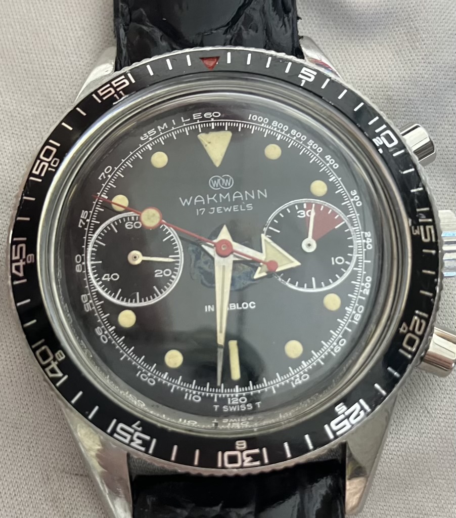 Wakmann chronograph watch with black dial, two subdials, red hands, and a tachymeter bezel with white numerals on a black ring.